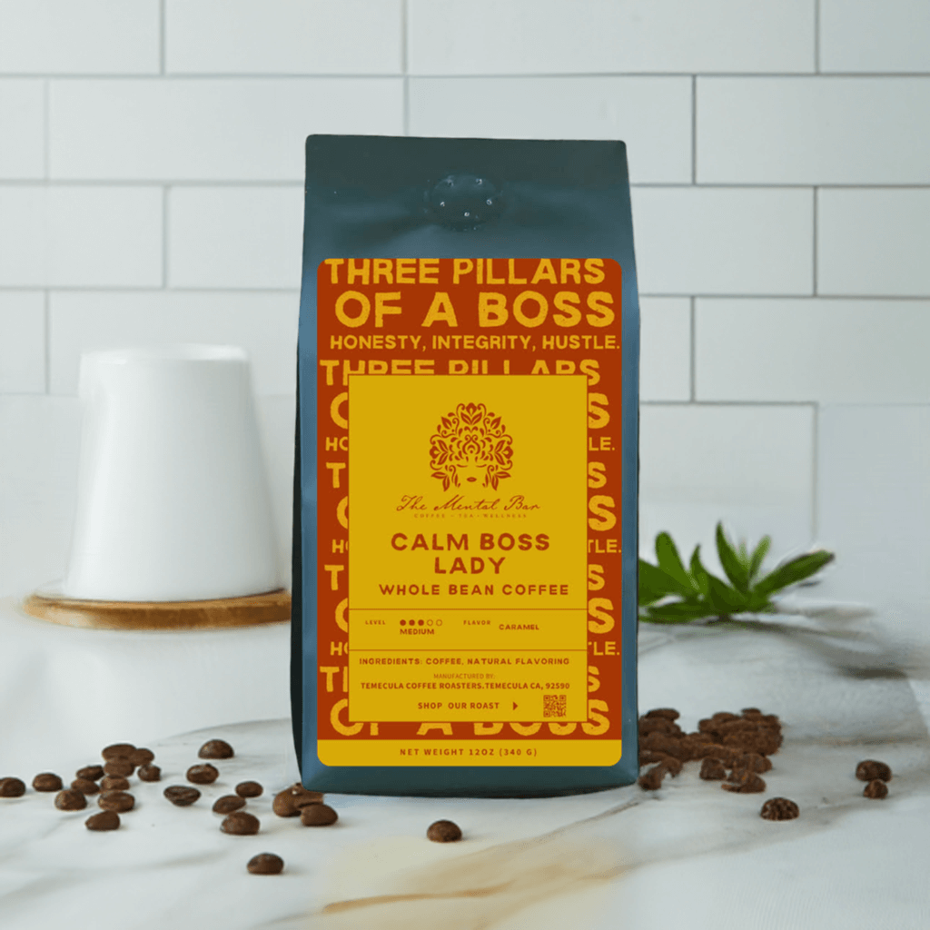 A bag of 'Calm Boss Lady' whole bean coffee with a yellow and black label, placed on a white surface with a ceramic cup and coffee beans scattered around.