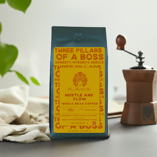 A bag of Hustle & Flow whole bean coffee with a yellow label, placed in front of a wooden coffee maker and a plant, on a table with a cloth.