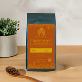 A bag of Metro Blend coffee with a label that showcases the brand, product name, and additional details, placed on a wooden surface next to a plant and a wooden spoon.