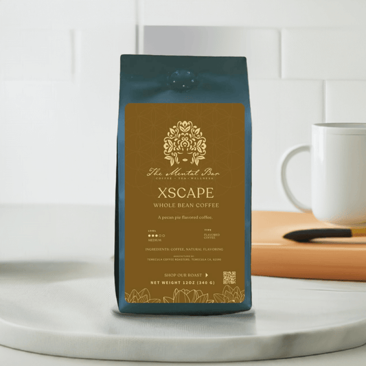 A bag of 'The Mental Bar' Xscape Whole Bean Coffee, with a medium roast level, displayed on a kitchen counter with a mug and a pen in the background.